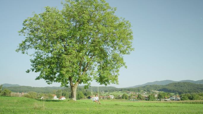 慢动作：春天阳光明媚的日子，一对快乐的年轻夫妇在绿树下摇摆。女朋友和男朋友享受浪漫的夏日。年轻男女在