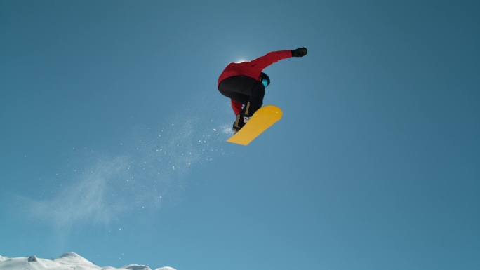 慢动作特写：在阳光灿烂的高山荒野中，极限运动的滑雪者跳过蔚蓝的天空。 在高山滑雪胜地,自由式滑板滑雪