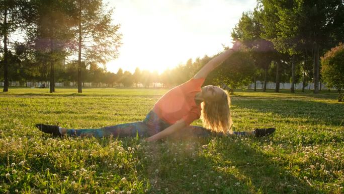 在一个城市公园里, 女子体操运动员坐在草地上, 做伸展运动