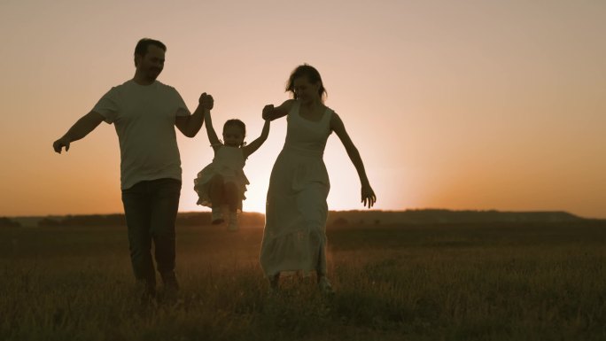 和爸爸妈妈在日落的时候跑过田野，快乐的家庭，和父母一起过着快乐的生活，和父母一起跑着去散步，积极的生