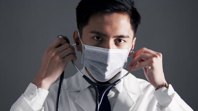 亚洲的年轻医生穿着白色的医疗外套，手持听诊器