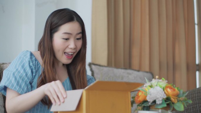 快乐而兴奋的亚洲女性顾客坐在沙发上，打开收件箱，对网上购物订单在家里送达感到满意。