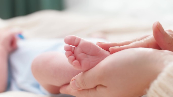小婴儿的脚在女性的手中。年轻的母亲轻轻地触摸和抚摸她新生的小腿。家庭幸福和有年幼子女的慈爱父母的概念