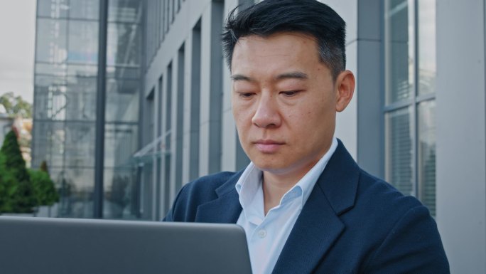 关闭亚洲40多岁的商人企业家雇主男性员工经理老板设计金融分析师在城市室外从事电脑打字远程在线工作网络