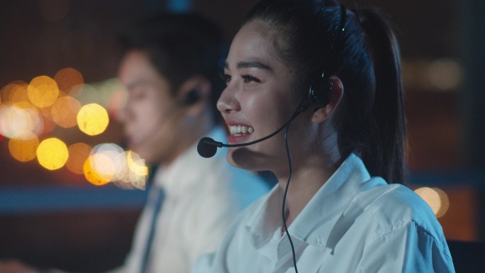 千年亚洲青年呼叫中心团队或客户服务主管在深夜办公室使用电脑和麦克风耳机提供工作技术支持。电话推销或销