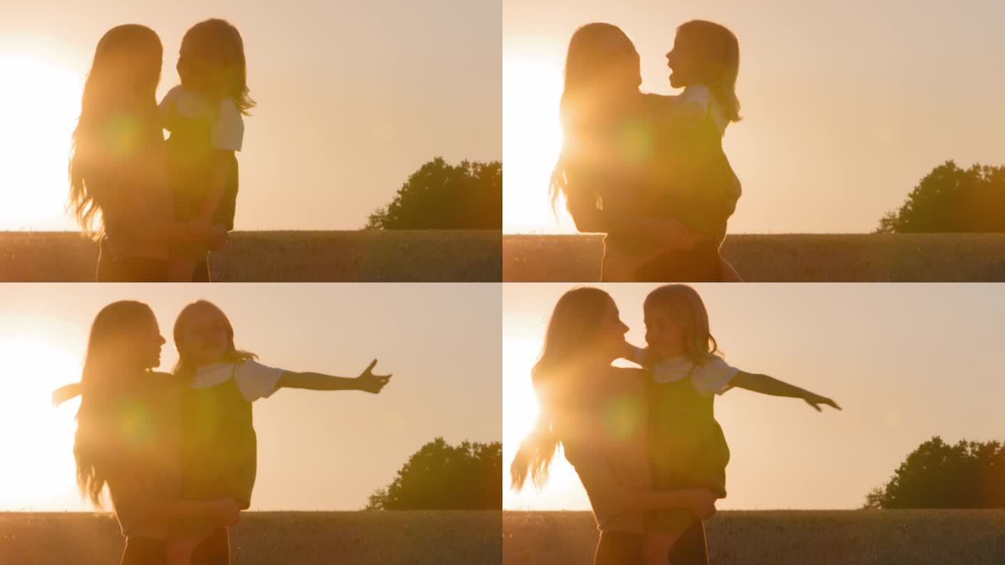 两名轮廓女性在日落时分抱着小女孩在阳光下妈妈抱着小女儿玩飞机机翼飞机飞行员假装在户外麦田里用手玩乐