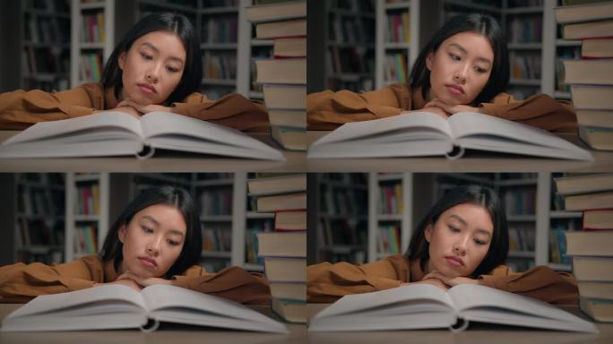 无聊悲伤疲惫懒惰的年轻韩国女子读无聊的书躺在大学图书馆的桌子上没有动力做作业的女学生为大学考试做准备