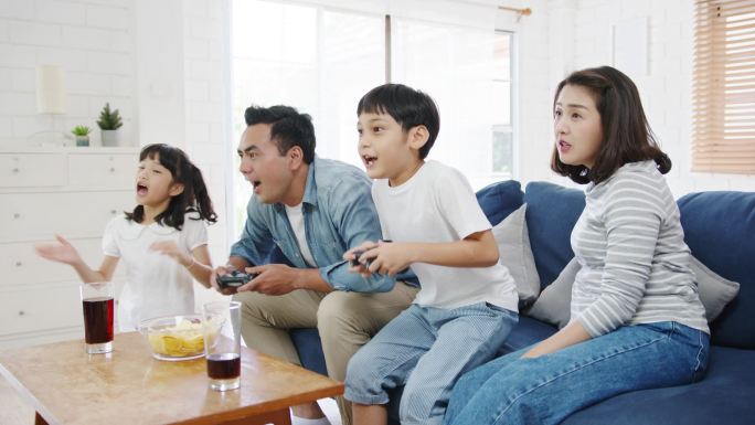 快乐的亚洲家庭爸爸，妈妈和孩子们在家里客厅里玩着技术控制台的电子游戏。自我隔离、待在家里、与他人保持