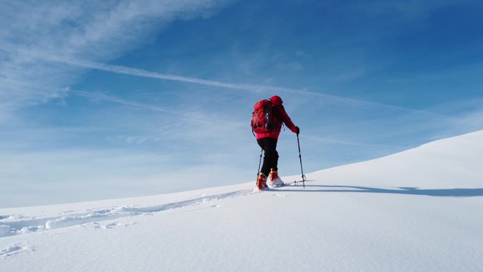 滑雪登山者爬上蓝天之上的雪山. 冬季，阳光灿烂的日子。 概念：实现个人目标、探索、新的视野.