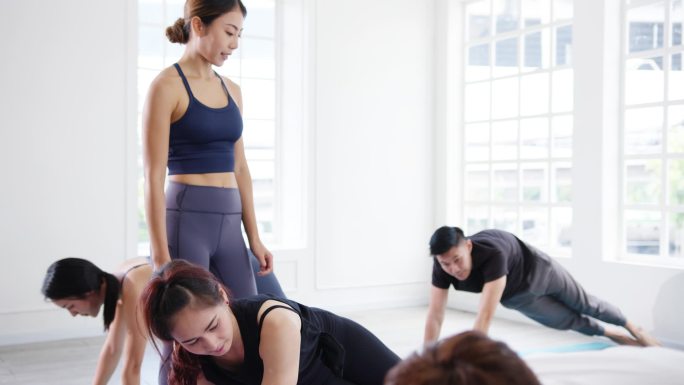 年轻有魅力的亚洲运动员和教练一起练习瑜伽。在健身室锻炼健康生活方式的亚洲妇女群体。体育活动、体操或芭