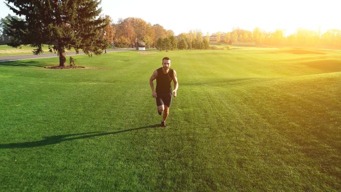 那个人在阳光灿烂的背景下在一个美丽的公园的草地上奔跑