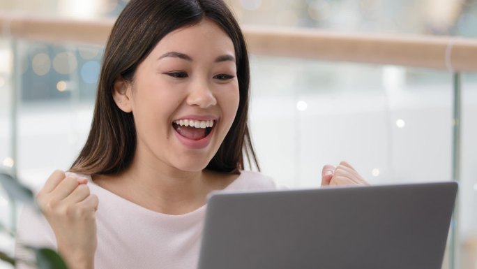 韩国亚洲女子用笔记本电脑幸运兴奋惊讶感到非常高兴获得大学奖学金赢得在线拍卖胜利赢得情感女性获胜者庆祝