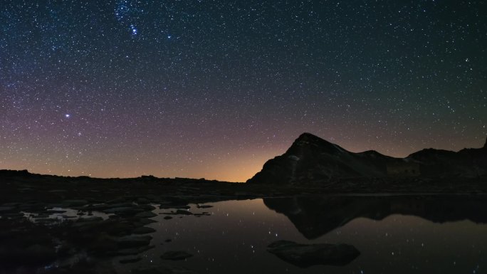 表观旋转的银河和满天星斗的天空，白雪皑皑的山山脊那边反映田园木条的湖面上。时间间隔4 k视频。