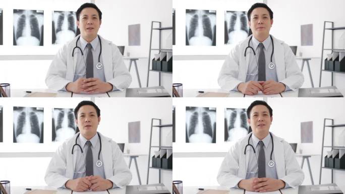 年轻的亚洲男医生身穿白衣，带听诊器，用电脑笔记本电脑与病人交谈视频电话会议，在保健医院看相机。咨询和