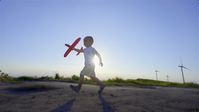 小男孩拿着飞机模型逆光奔跑在山顶追求梦想