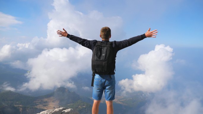 徒步旅行者背着背包站在山边，举起双手享受自由。人类在探索新地方的过程中积极地休息。游客们欣赏山顶上的