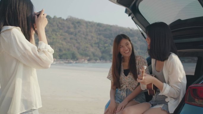 在海滩暑假期间，年轻女性组成的快乐之友小组在后备箱中自由地弹奏四弦琴唱歌，并与智能手机合影，乘车旅行
