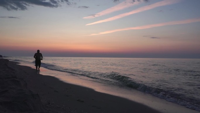 在日出时分，一个人平静地沿着荒芜的海滩走着。海景
