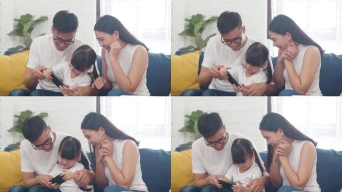 快乐的亚洲家庭爸爸、妈妈和女儿在网上玩着好玩的游戏、坐在家里的沙发上。自我隔离、待在家里、与他人保持