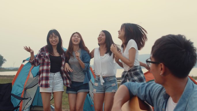 亚洲最好的朋友组青少年在国家公园的帐篷旁一起击掌和跳舞，享受吉他音乐的快乐时光。背景上美丽的自然，山