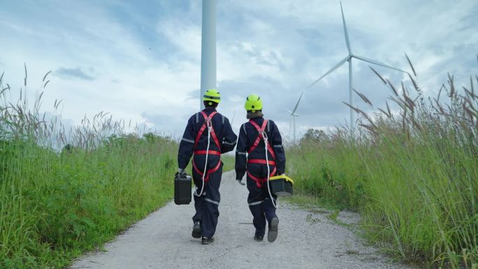 两名从事安全设备维修工作的工程师步行到风力涡轮机前，检查风力涡轮机的运行情况，清洁能源概念，可再生能