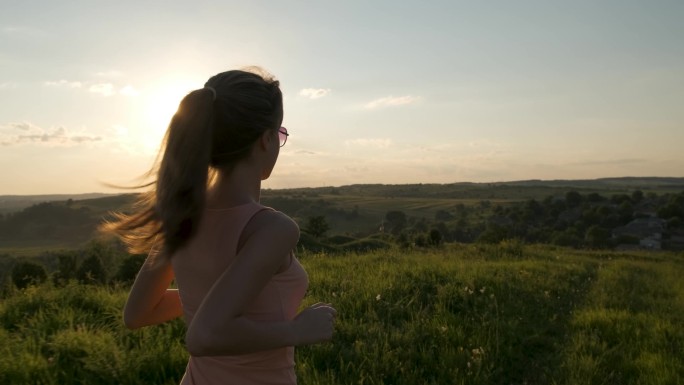 穿着粉红衣服的年轻女子在温暖的夕阳西下的草地上奔跑.