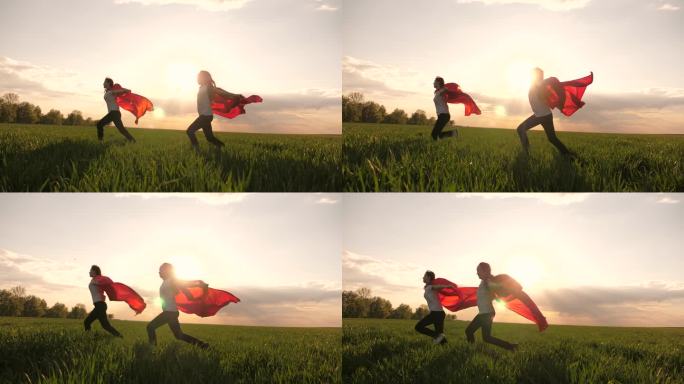 快乐的女孩扮演超级英雄，她们穿着红色斗篷在绿地上奔跑，风中飘扬着斗篷。孩子们的游戏和梦想。慢动作青少
