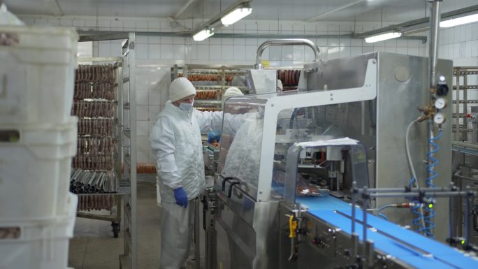 香肠部门的工作人员站在真空包装香肠的自动包装装置旁边.