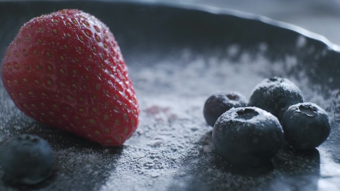 用蓝莓在草莓上撒些糖粉.