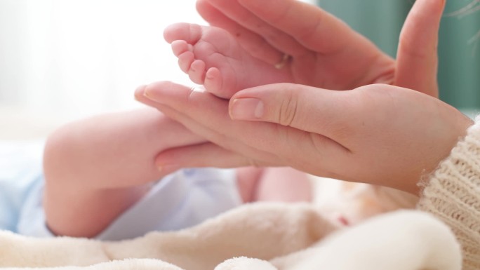 母亲触摸和抚摸新生婴儿小脚的特写镜头。家庭幸福和有年幼子女的慈爱父母的概念。婴儿按摩和保健