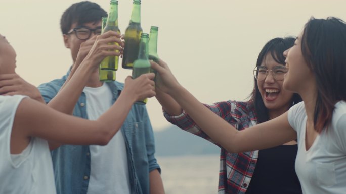 一群亚洲最好的朋友青少年跳舞和喝酒享受快乐的礼炮瓶啤酒敬酒在营地一起享受快乐时光。背景是美丽的自然、