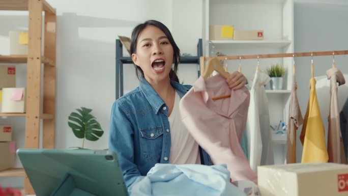 年轻的亚洲女士时装设计师使用手机接收订购单，并在商店网上直播服装录像。小企业主，网上市场交付概念.