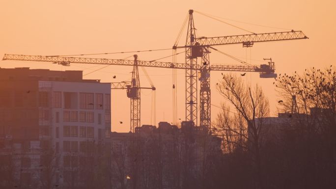 夕阳西下高楼建筑工地塔式起重机的黑暗轮廓.房地产开发