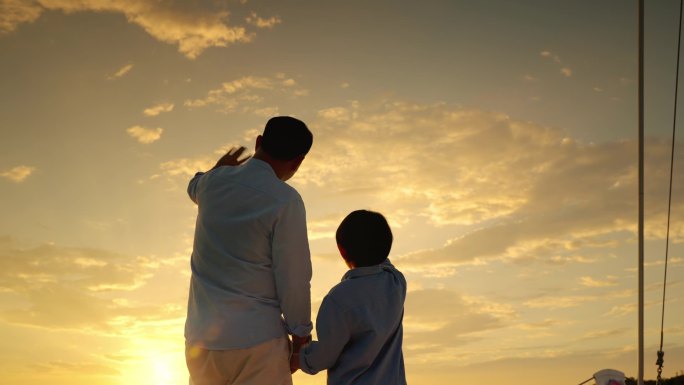 在日落的时候，父亲和儿子在游艇上挥手致意。亚洲家庭关系