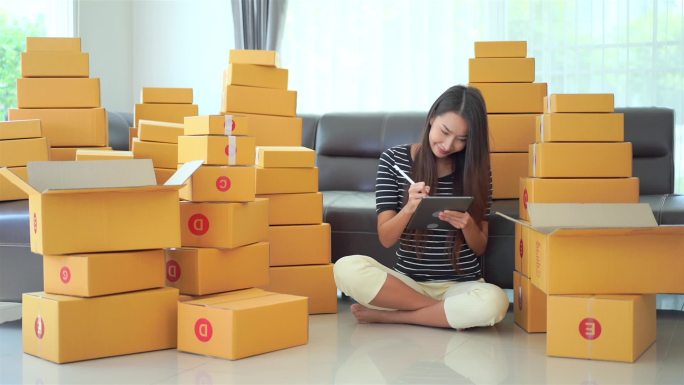 美丽的亚洲女人在家里拿着盒子里的包裹工作的镜头