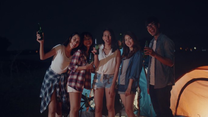 亚洲最好的朋友组青少年拍照片记忆舞蹈和喝酒有趣的礼炮瓶啤酒敬酒晚上在露营地一起享受快乐时刻的聚会。美
