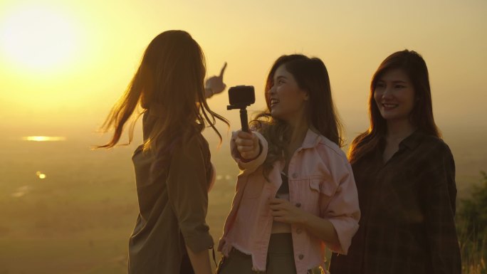 在夕阳西下，亚洲人站在那里观看大自然的美丽，并从他们的动作片中拍摄视频，向他们的朋友展示社交媒体、自