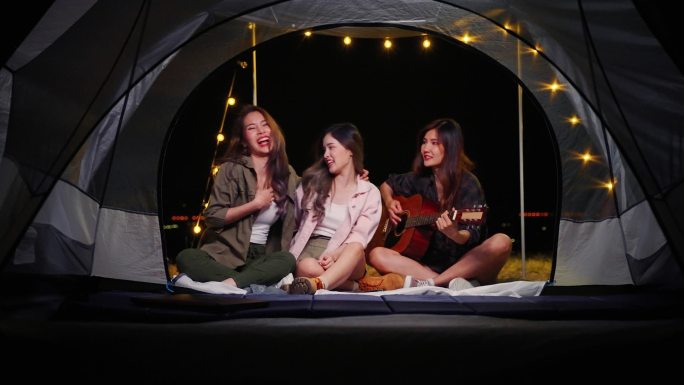 一群年轻的亚洲朋友在夏令营期间弹吉他，在帐篷里唱歌。自由,休闲,旅行,冒险的概念