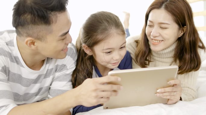  快乐的家庭在家里的卧室里使用数码平板电脑