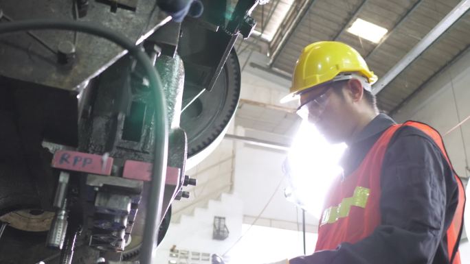 亚洲工人在金属板制造厂生产线上操作冲压机，穿着安全玻璃制服和安全帽。夜间大灯，以确保良好的外观检查质
