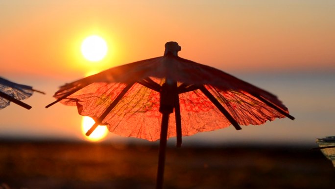 日落时分，海滨沙滩上的纸制鸡尾酒雨伞.