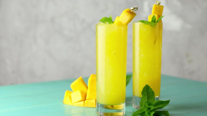 新鲜的夏季冰凉芒果鸡尾酒与薄荷和芒果。新鲜的芒果汁在浅蓝色的背景上缓缓流动