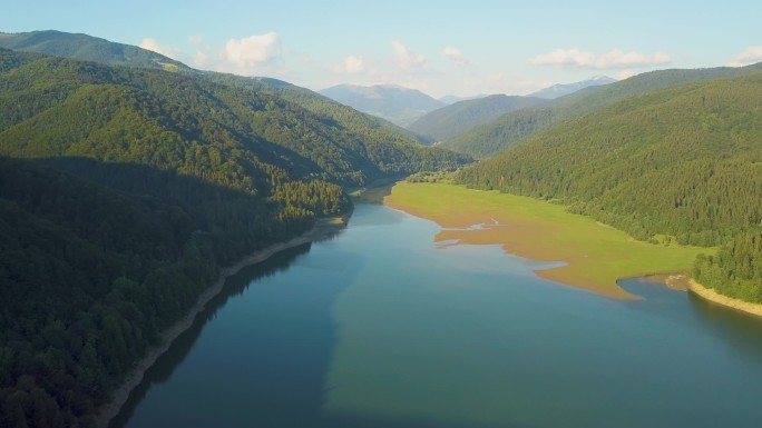 高山峻岭间覆盖着茂密的常绿森林，空中俯瞰蓝水清澈的大湖泊.