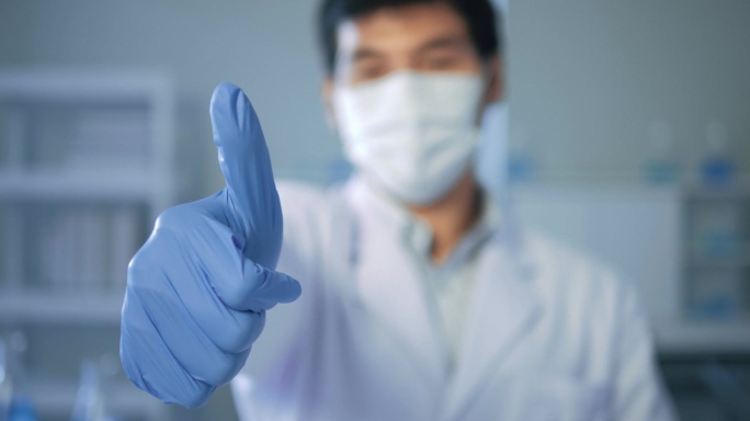 亚洲男性医生，戴口罩的科学家，在实验室试管蓝色液体的照相机前竖起大拇指。医疗科学保健概念.