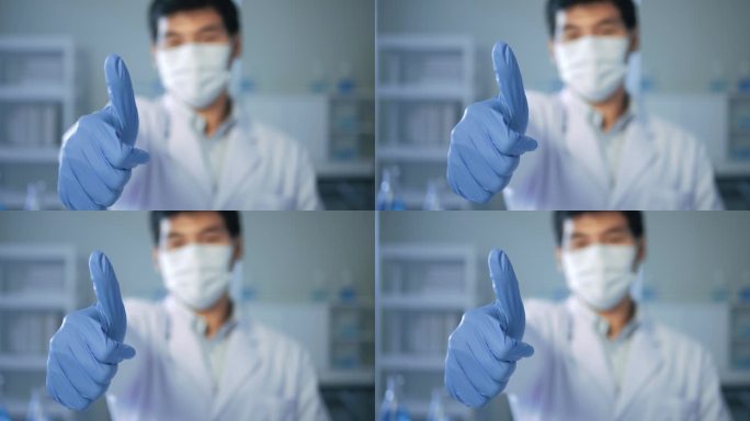 亚洲男性医生，戴口罩的科学家，在实验室试管蓝色液体的照相机前竖起大拇指。医疗科学保健概念.