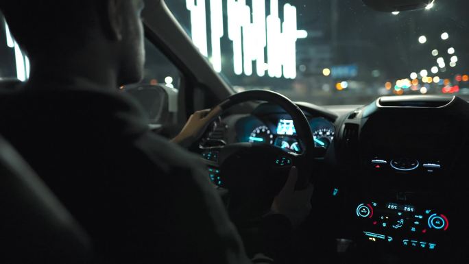 男人开车穿过夜城的街道。从车子的后座上看.