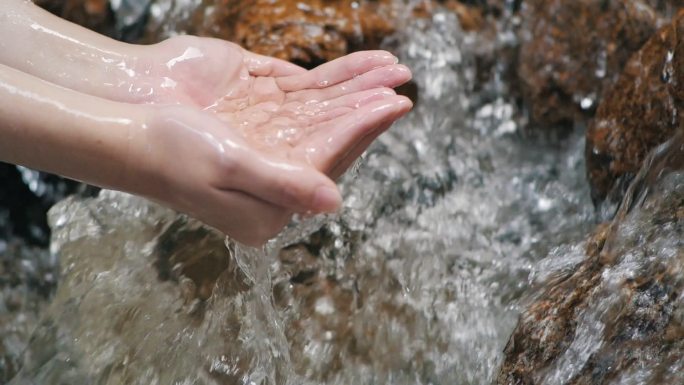 手握干净的飞溅瀑布在森林的河流或湖中。清澈的水花倒入手心里.水滴，水资源，土地，环境。保护自然资源.