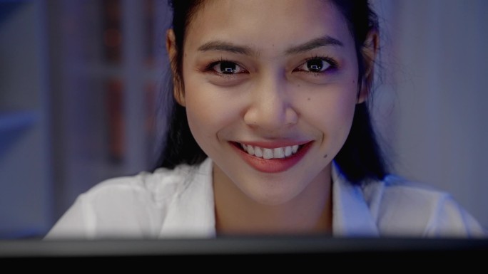 特写，亚洲女人在夜间在电脑显示器前微笑.