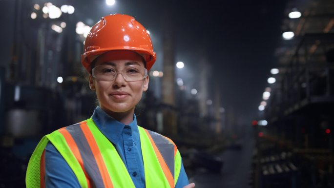 在巨大的工业仓库里戴安全帽的女工程师笑着相机.