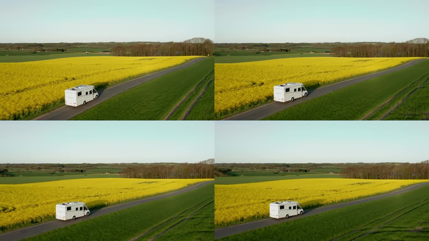 在晴朗的蓝色日子里，一架无人驾驶飞机从后面跟随一辆棕色货车。车轮上的大篷车沿着被大自然包围的道路移动